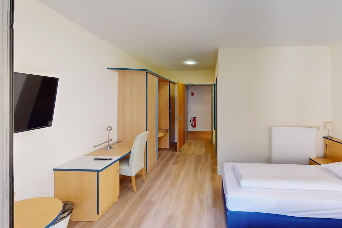Habitación de hotel con cama, escritorio, silla, televisor y extintor.