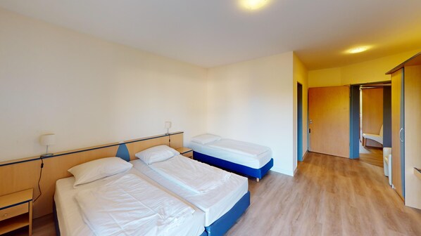 A hotel room with two beds, a nightstand, a lamp, and a wardrobe.
