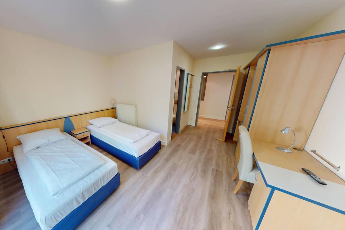 Una habitación de hotel con dos camas, un escritorio, una silla y un armario.