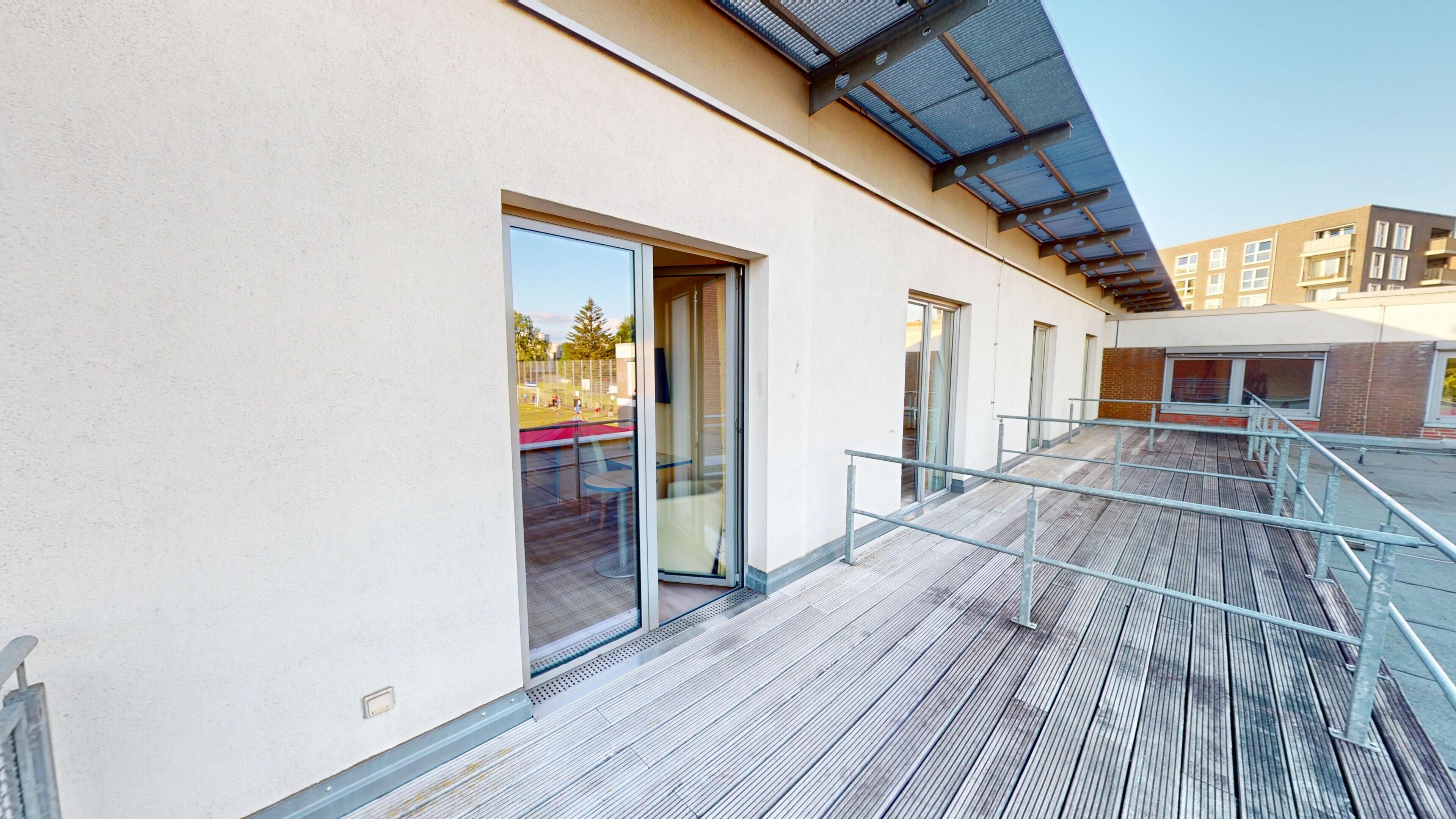 Un bâtiment moderne doté d’une terrasse en bois, de portes vitrées et d’une rambarde en métal.