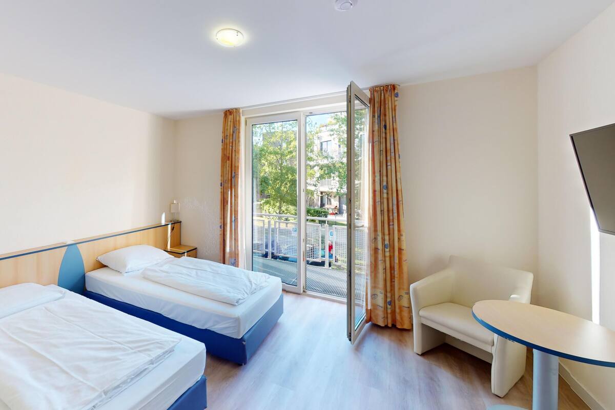 Habitación de hotel con dos camas, televisión, una mesita y balcón con vistas.