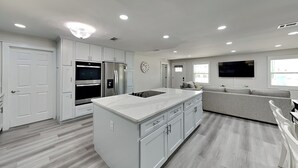 A modern kitchen with white cabinetry, a central island, and built-in appliances. - Turtle Dove | Five Min Walk to Beach, Large Fenced Yard (Panama City)