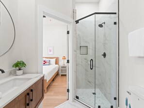 Une salle de bain moderne avec une douche à parois de verre, un lavabo blanc agrémenté d’une plante en pot et un meuble en bois.