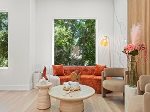 Un salon moderne comprenant un canapé, des fauteuils, une table basse et une grande fenêtre donnant sur un paysage arboré.