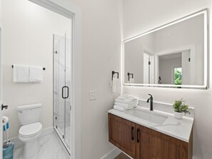 A modern bathroom with a toilet, shower, vanity, and a large mirror. - 3014 Coral Blossom A | 0.3mi to Beach, Game Room (Panama City Beach)