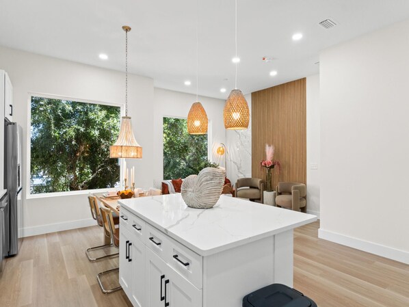 Une cuisine moderne avec des meubles blancs, un plan de travail en marbre et des luminaires suspendus.