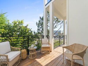 Una terraza de madera con mobiliario de mimbre, una mesa de vidrio y vistas a un paisaje urbano.
