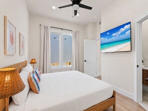Ein Schlafzimmer mit einem Bett, einem Deckenventilator, einem Fernseher und einem Fenster mit Vorhängen.