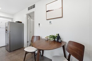 Ein Essbereich mit einem runden Holztisch, zwei Stühlen, einer Topfpflanze und einem an der Wand befestigten Lichtschalter.