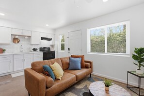 Eine moderne Küche mit weißen Schränken, einem braunen Ledersofa mit Kissen, einem runden Couchtisch und einem Blumentopf.