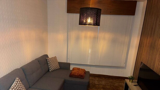 Ein modernes Wohnzimmer mit einem grauen Sofa, einem braunen Teppich, einer Holztv-Konsole und einer schwarzen Pendelleuchte.