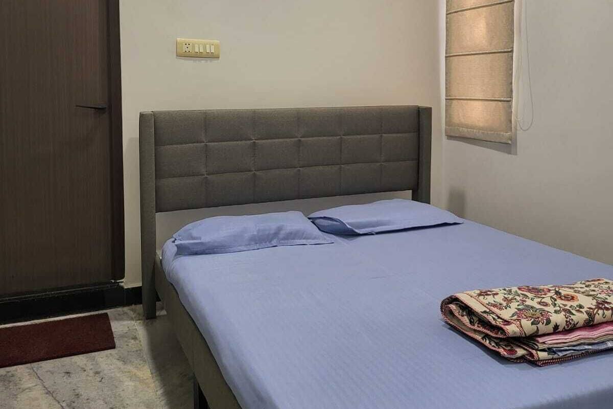 A bedroom with a bed, an air conditioner, a door, and a window with blinds.