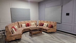 A sectional sofa with a wooden coffee table in a room with light-colored walls and a marble floor.