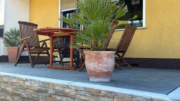 Un patio con una mesa y sillas de madera, una planta grande en maceta y un muro de piedra.