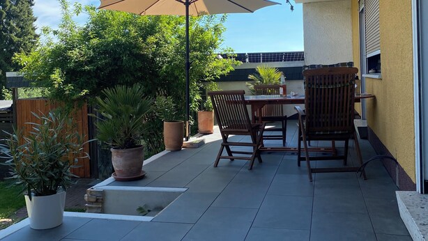 En terrasse med bord og stole, plantekrukker og en stor parasol.