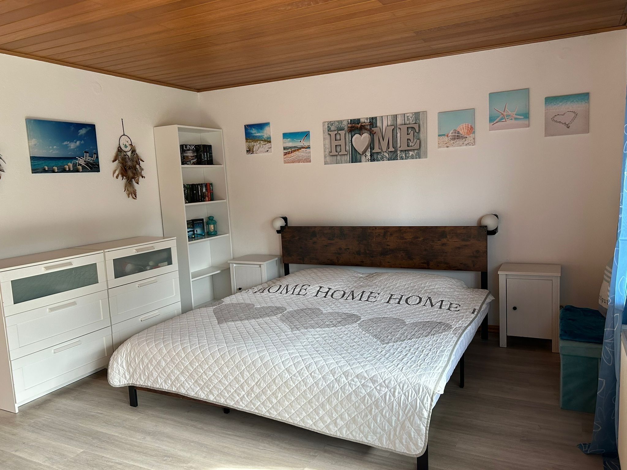 Um quarto com uma cama, penteadeira, estante e obras de arte nas paredes.
