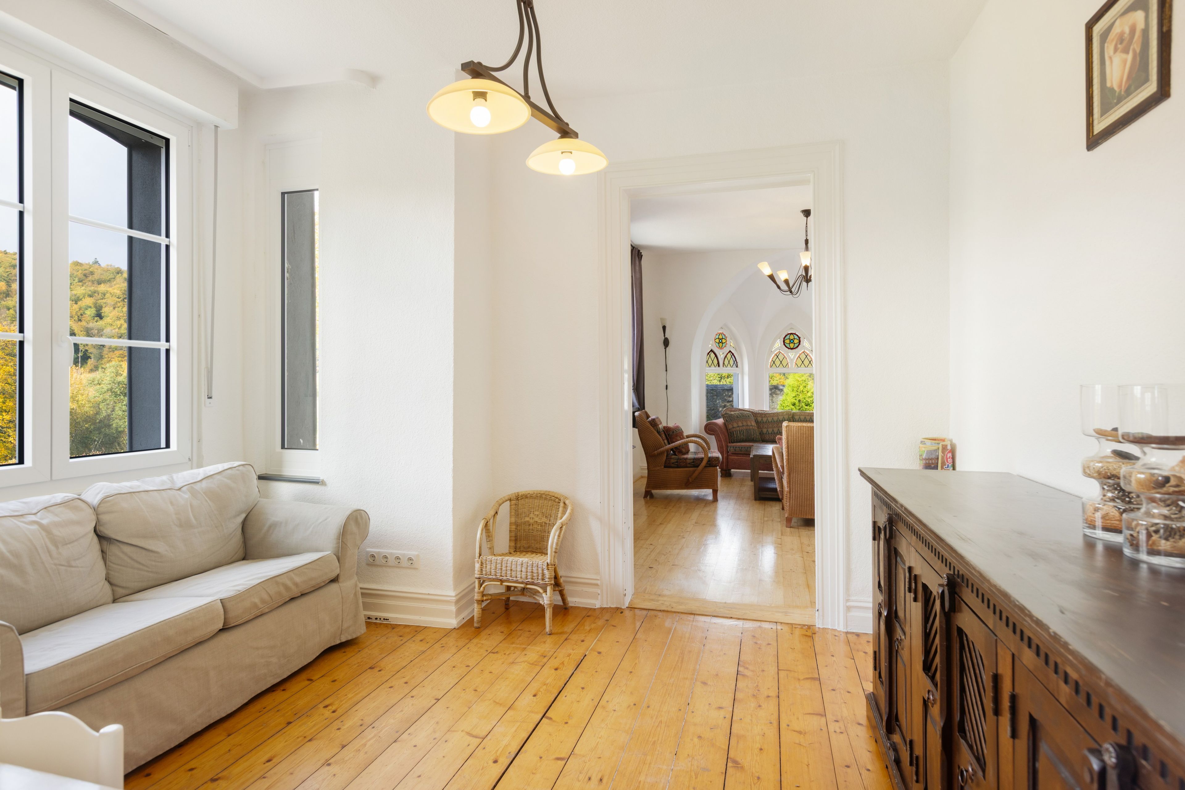 A room with a wooden floor, a sofa, a chair, a dining area with a table and chairs, and a kitchen area with a wooden cabinet.