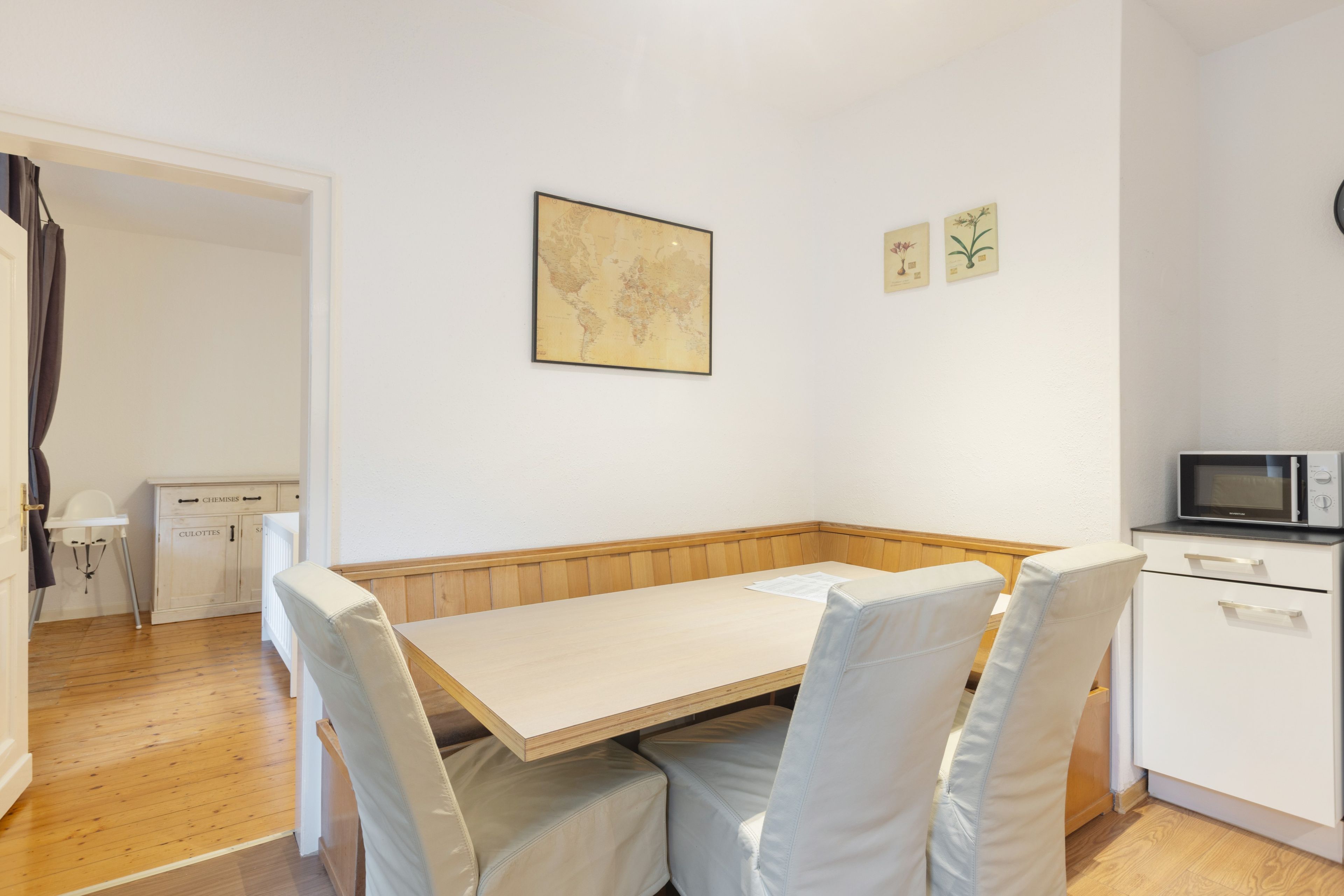 Un comedor con una mesa de madera y sillas acolchadas, un mapa en la pared y un microondas en la esquina.