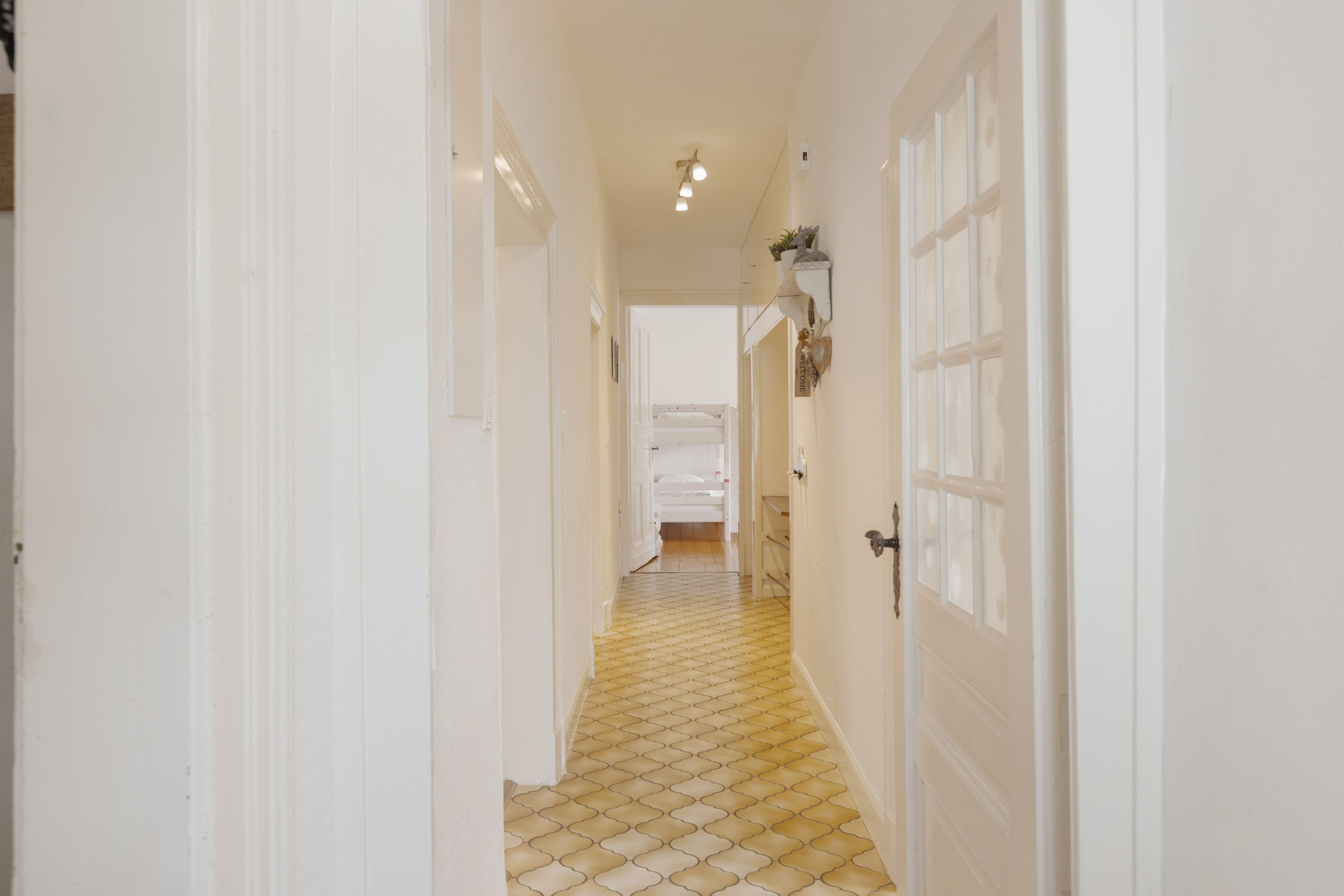 A hallway with white doors, a tiled floor, and a bed in the distance.