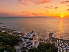 A coastal hotel with a view of the sunset over the sea, a parking area, and a building with multiple floors. - Sea Breeze Apartment with Balcony (Durres)