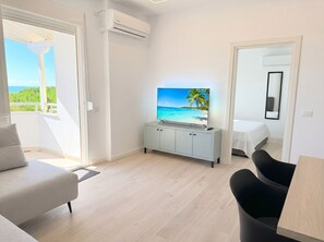 A modern hotel room with a balcony, a flat-screen TV, a bed, and a dining area. - Sea Breeze Apartment with Balcony (Durres)