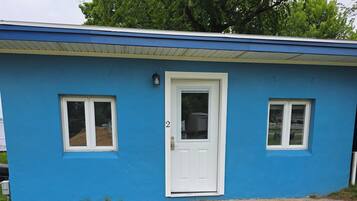 Un petit bâtiment d’un seul étage, à l’extérieur bleu, avec une porte blanche et deux fenêtres.