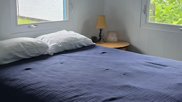 Une chambre à coucher avec un lit, deux fenêtres équipées de stores, une table de chevet avec une lampe et un tableau encadré.