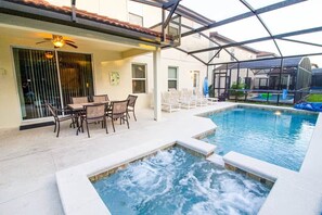 Una piscina con hidromasaje, asientos exteriores y un patio cubierto.