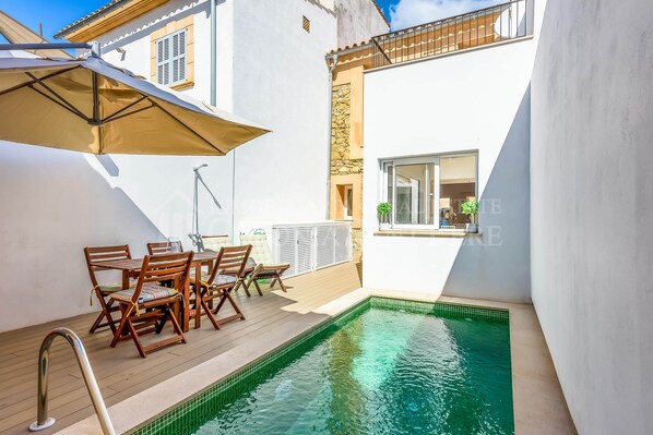Ein Poolbereich mit Tisch und Stühlen, ein kleiner Pool und ein Gebäude mit einem Fenster.