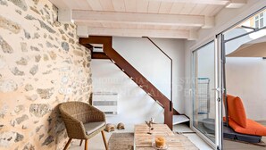 Un intérieur moderne avec des murs en pierre, des meubles en osier, une porte vitrée donnant sur l’extérieur et un escalier.