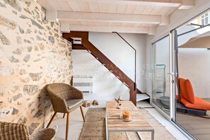 Ein modernes Interieur mit Steinwänden, Rattanmöbeln, einer Glastür, die nach draußen führt, und einer Treppe.