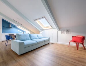 A modern loft apartment with a skylight, a light blue sofa, a red chair, and a kitchen area. - Casalina by Napoliapartments (Naples)