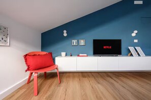A modern living room with a blue accent wall, a white entertainment unit, a red chair, and a flat-screen TV displaying 'NETFLIX'. - Casalina by Napoliapartments (Naples)