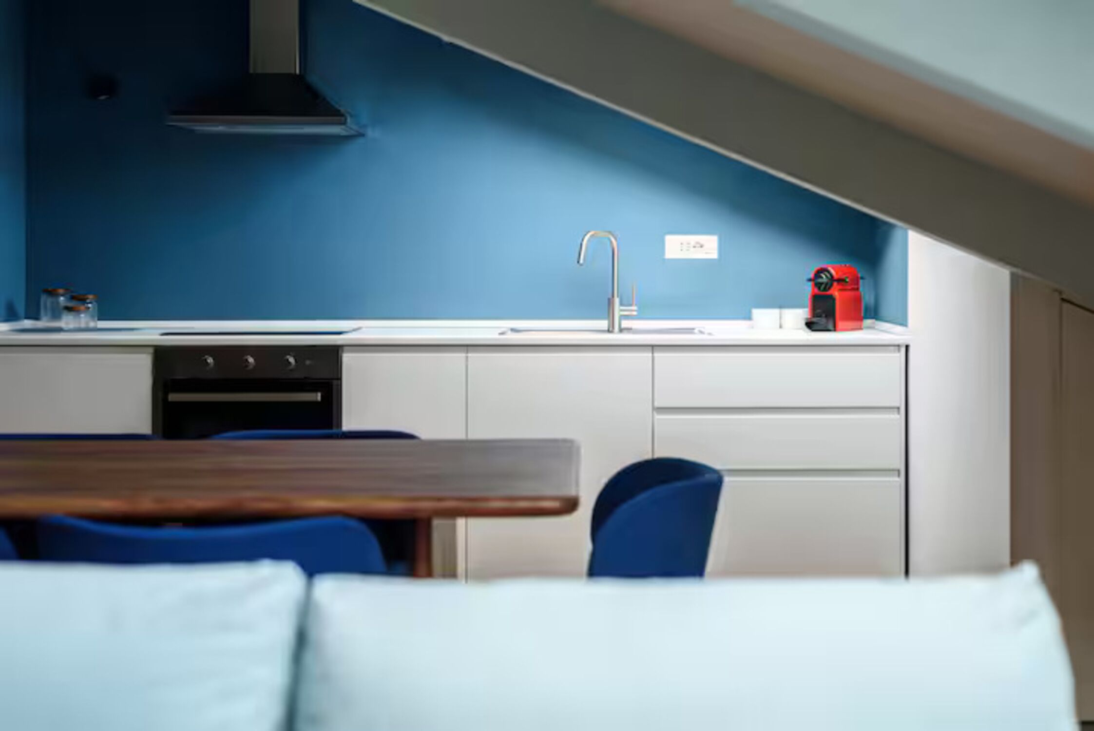 Een moderne keuken met een blauwe wand, witte kastjes, een spoelbak, een fornuis en een rode koffiemachine.