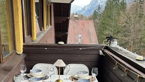 Ein Balkon mit Tisch für zwei Personen, einem Korbstuhl und Blick auf die Berge.