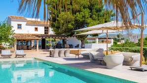 A poolside area with lounge chairs, a pergola, and a view of a white building with a tiled roof. - Vacation home Prana by Interhome (Moraira)
