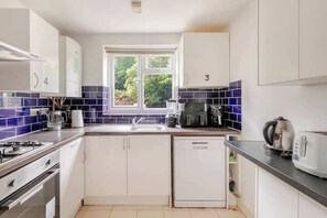Una cocina compacta con armarios blancos, lavavajillas integrado, estufa y ventana con vistas al verdor.