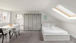 Ein Schlafzimmer mit Oberlicht, einem Bett, einem Schreibtisch mit Stühlen und einem Kleiderschrank.