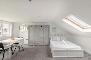 Un dormitorio con tragaluz, cama, escritorio con sillas y armario.