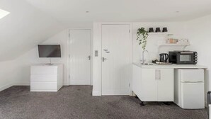 Ein kleiner, weißer Raum mit einer Küchenzeile, einem Flachbildfernseher, einem weißen Schrank und einer Tür mit Griff.