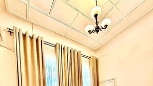 A room with two wooden beds, a chandelier, and a window with curtains. - Officers Boutique (Samarkand)