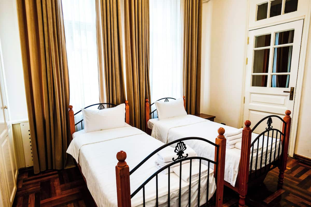 Una habitación con dos camas individuales, cabeceros de madera, una puerta blanca y una ventana con cortinas.
