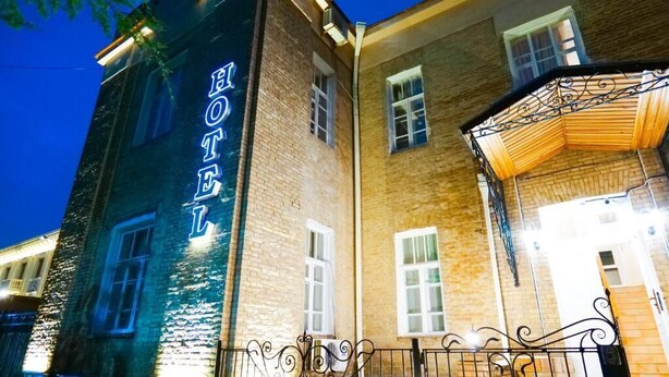 A hotel with a prominent 'HOTEL' sign, brick facade, and a balcony with wrought iron railing. - Officers Boutique (Samarkand)
