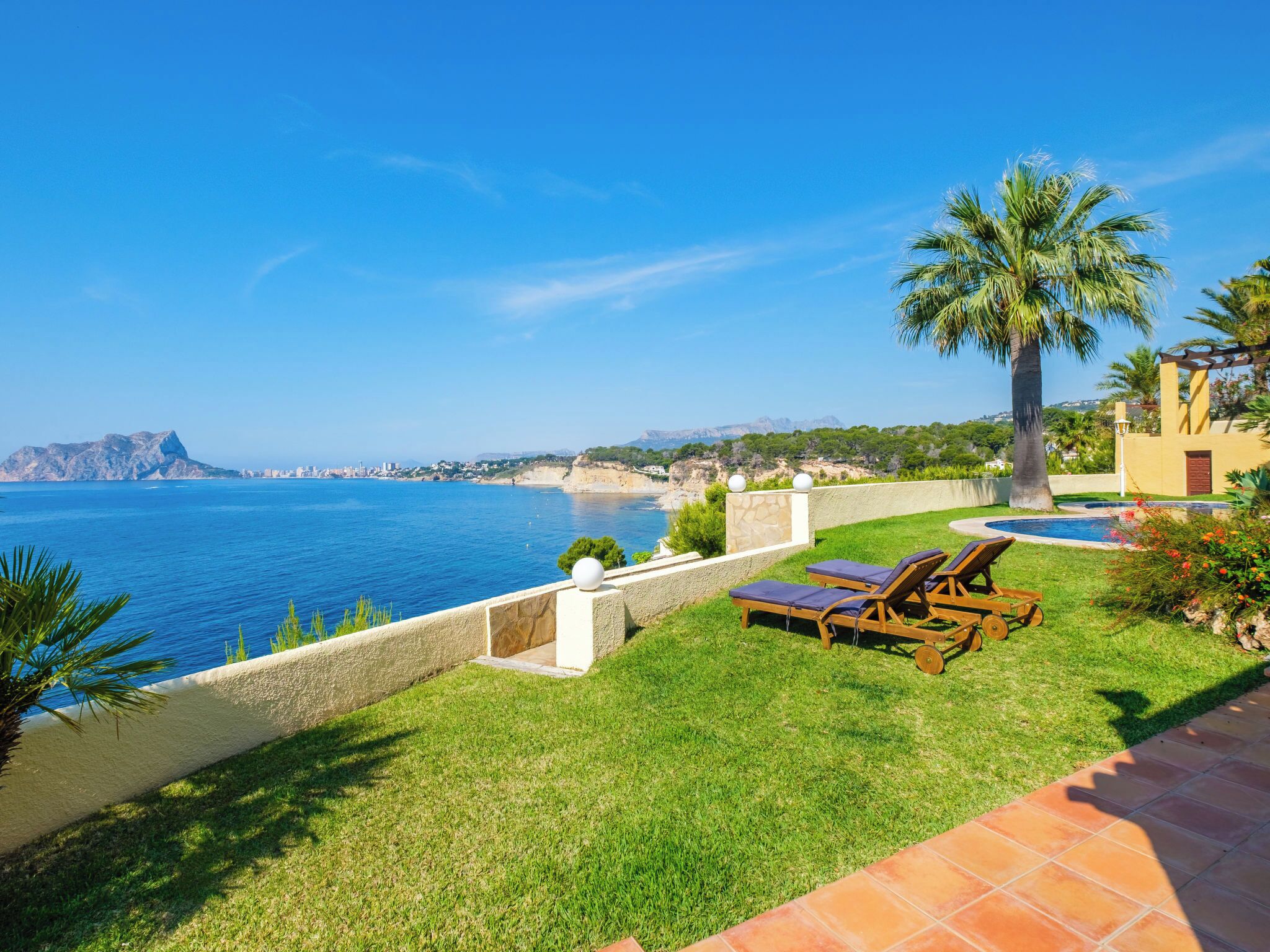 Une propriété située sur la côte, dotée d’une piscine, de chaises longues et offrant une vue sur la mer et les montagnes.