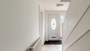 Een gang met een radiator, een witte deur met decoratief glas en een zwarte mat bij de ingang.