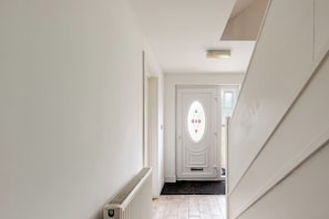 Un passadís amb un radiador, una porta blanca amb un detall de vidre decoratiu i un estri amb dibuixos a l'entrada.