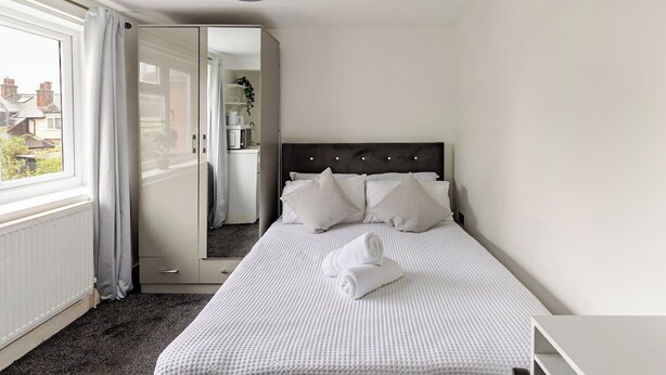 Een slaapkamer met een bed, een nachtkastje, een raam met gordijnen en uitzicht op buiten.