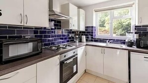 Een keuken met witte kastjes, een zwarte magnetron en een raam met uitzicht op groen.