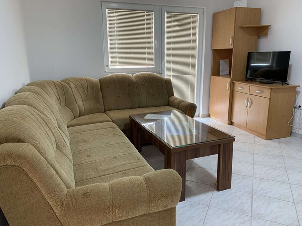 Ein Wohnzimmer mit einer Couch, einem Glastisch, einem Holzschrank und einem Fernseher.