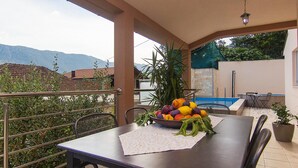 Un área de comedor al aire libre techada, con una mesa preparada para dos, un cuenco de fruta y vistas a montañas al fondo.